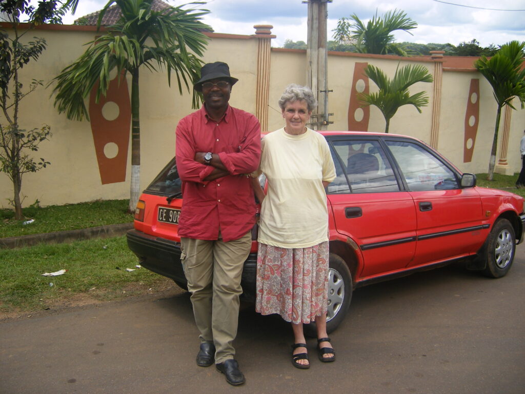 Two people standing in front of a red car. One on the left is a man, on the right, a woman.